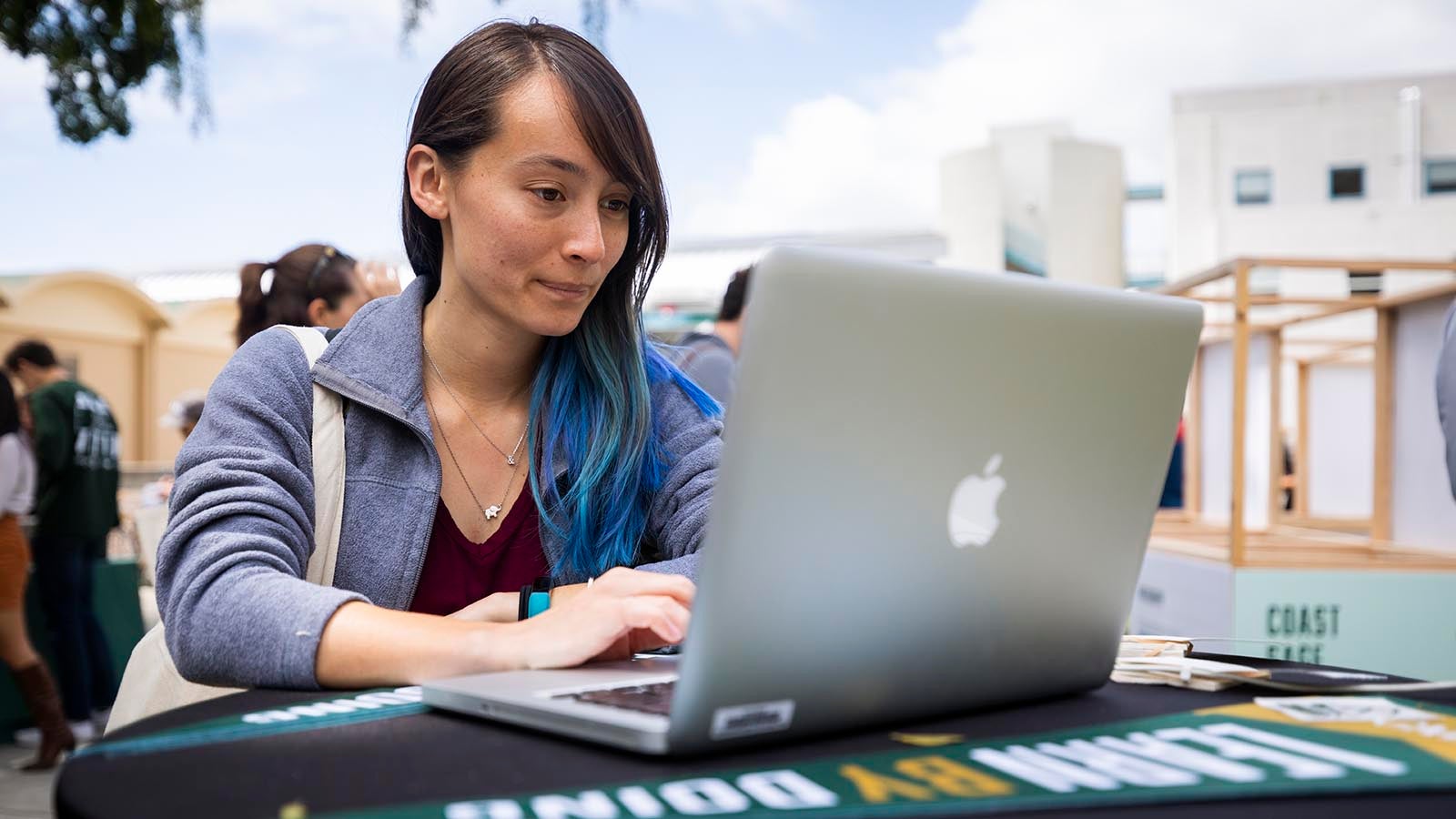 A student stands at a table outside on a laptop.