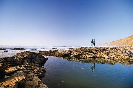Example of a wide shot with two people standing on rocks at a tide pool, staring out at the ocean. 
