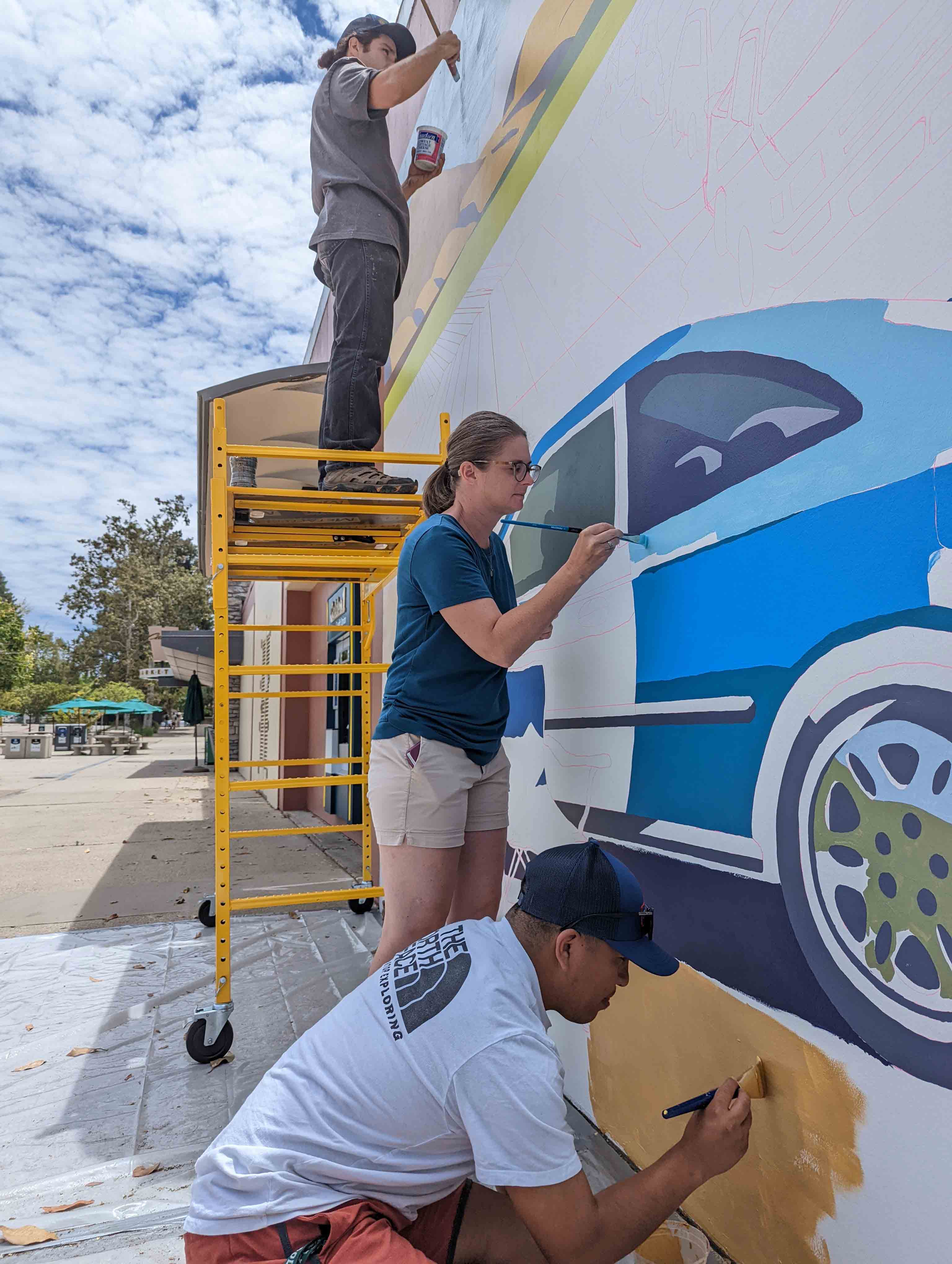 Three people painting the mural