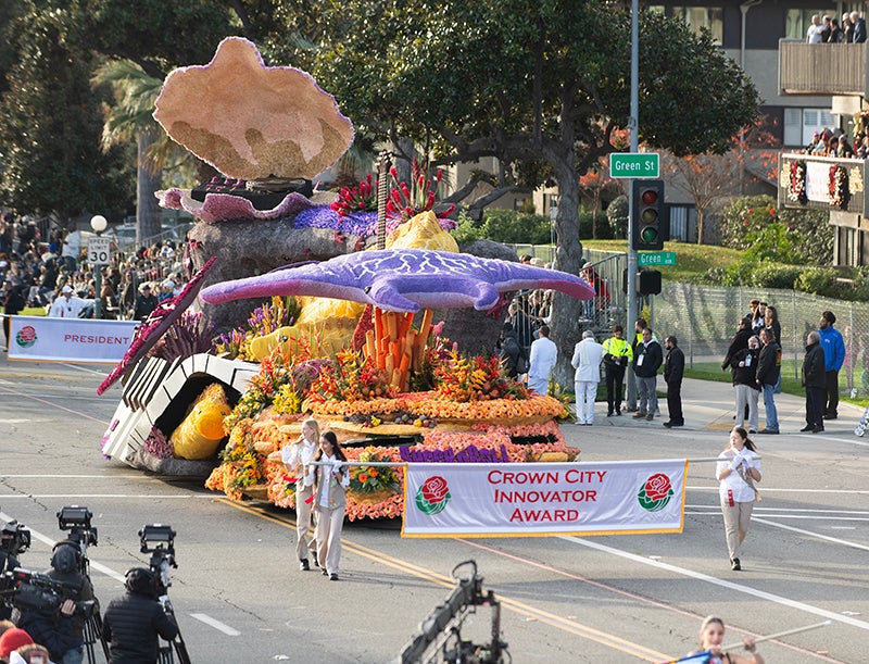 Rose Parade volunteers hold banner announcing Cal Poly universities float as Crown City Innovator Award recipient