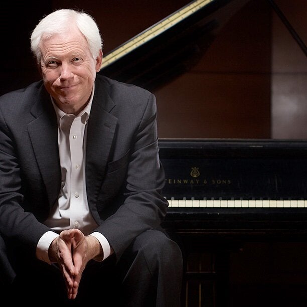 Pianist John Salmon seated on a piano bench with his back to the grand piano