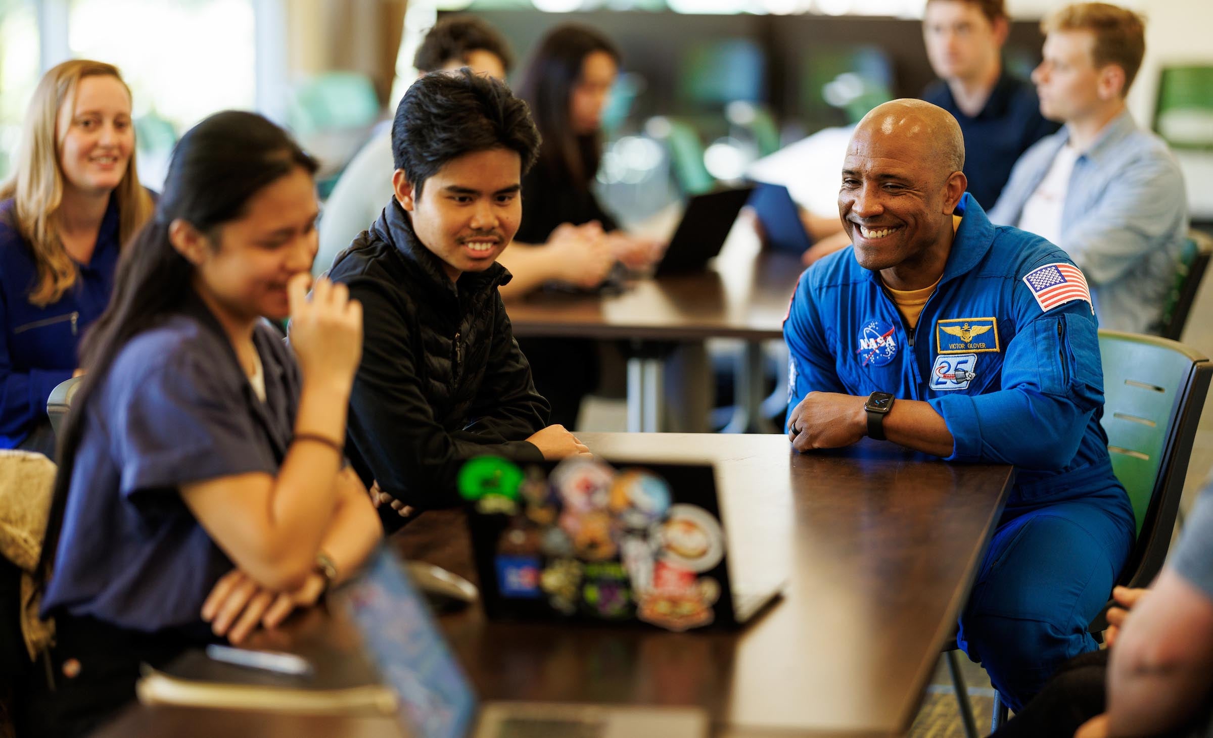 NASA astronaut and Cal Poly Alumnus Victor Glover smiles while watching a presentation on a laptop with students in an engineering group.