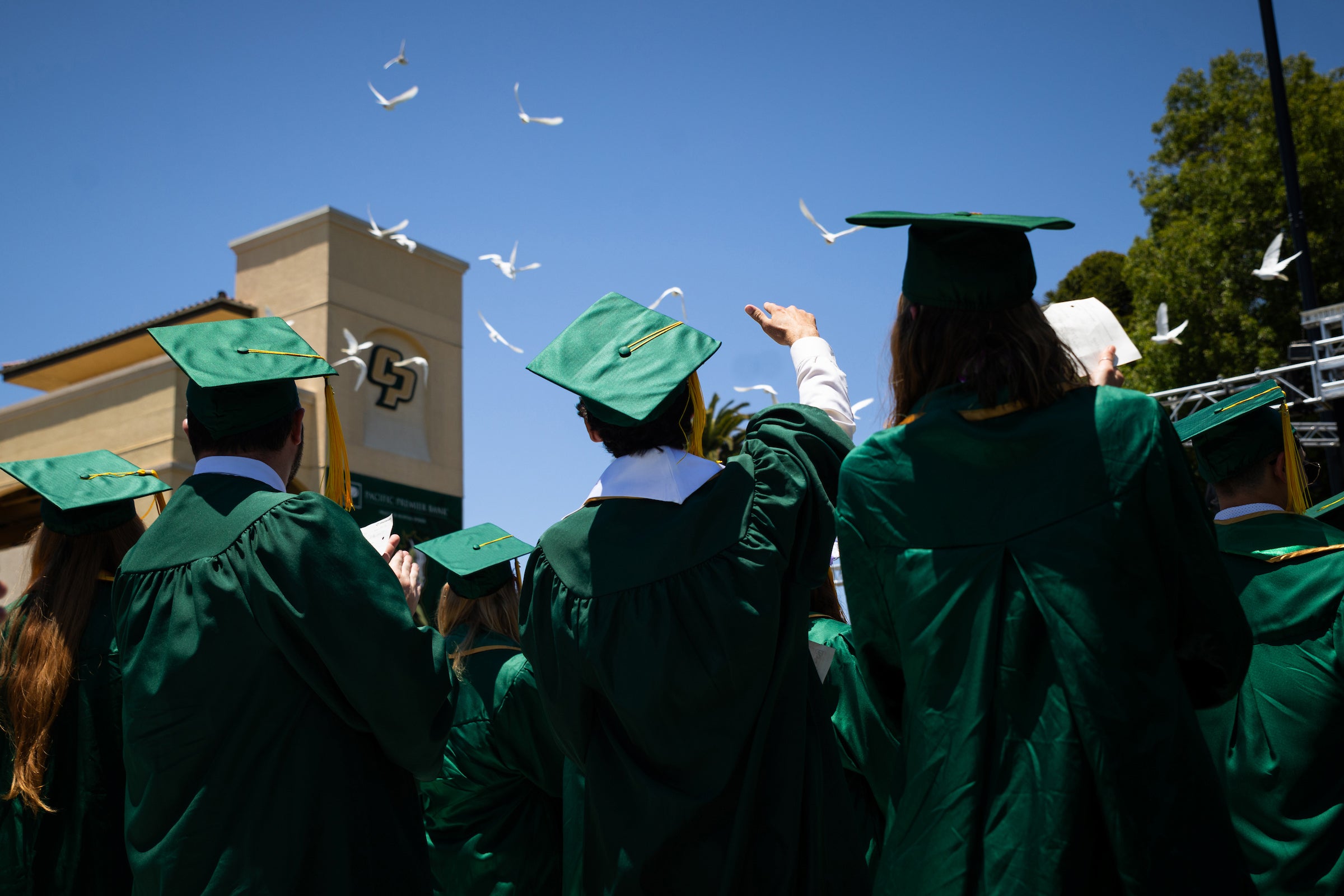 Cal Poly graduates in cap and gowns watch as doves take flight in Spanos Stadium