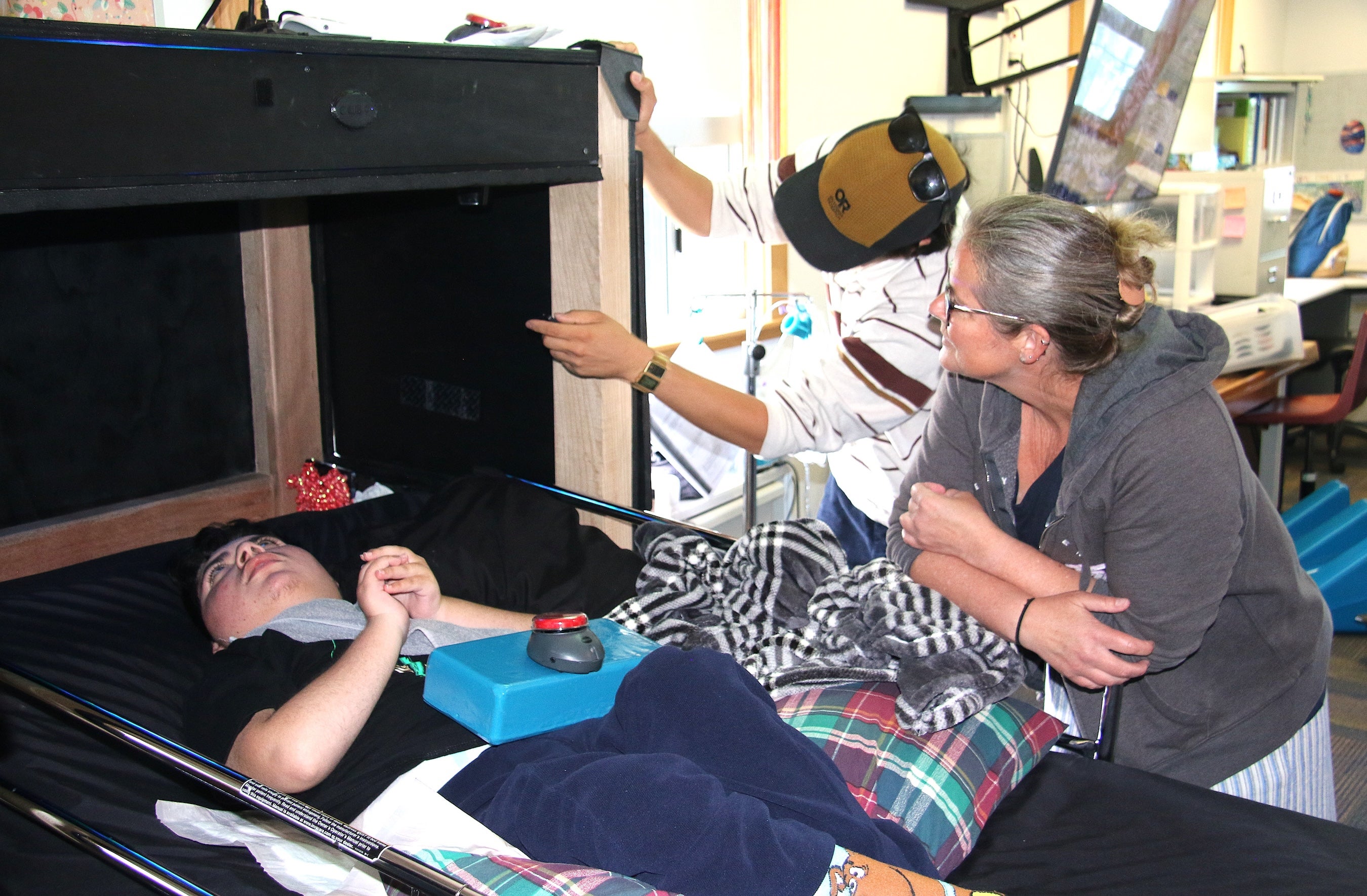 Marcus Kanenaga walks Heather McColley through the sensory den as Evan experiences the moving lights from a hospital bed in McColley’s classroom.