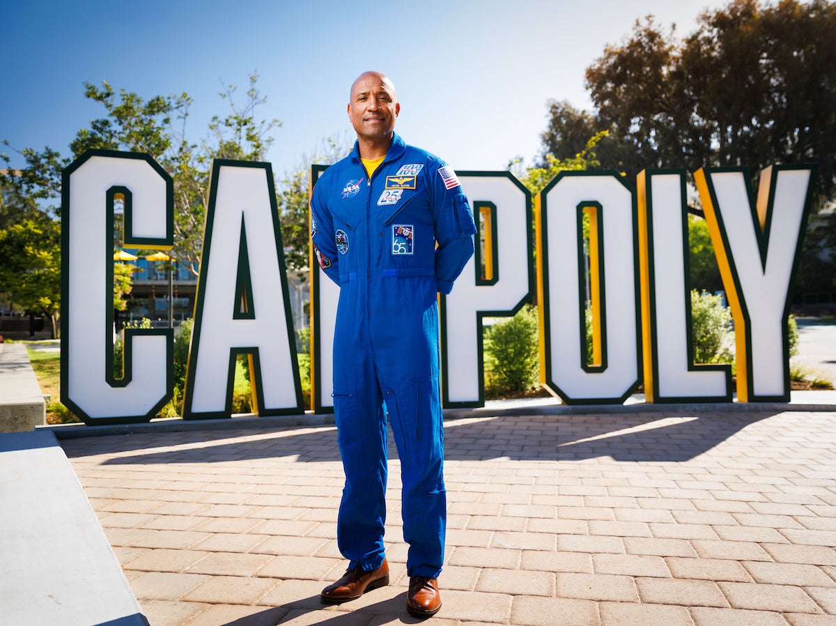 Victor Glover stands in front of large letters that spell "Cal Poly" on Cal Poly's campus. 
