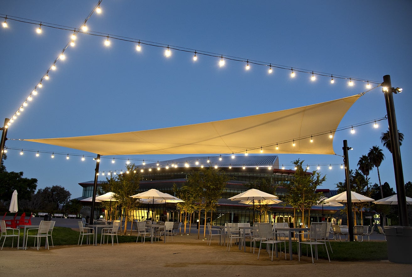 Tables and chairs sit on a veranda near the Performing Arts building under strings of white lights