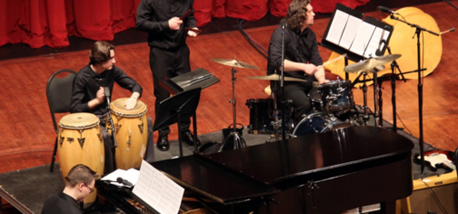 A jazz ensemble features four performers on piano and percussion instruments all looking to their left