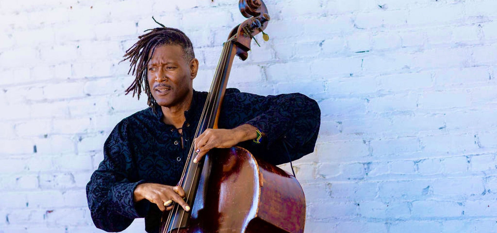 Bay Area bassist, bandleader, composer and educator Marcus Shelby plays bass in front of a white brick wall