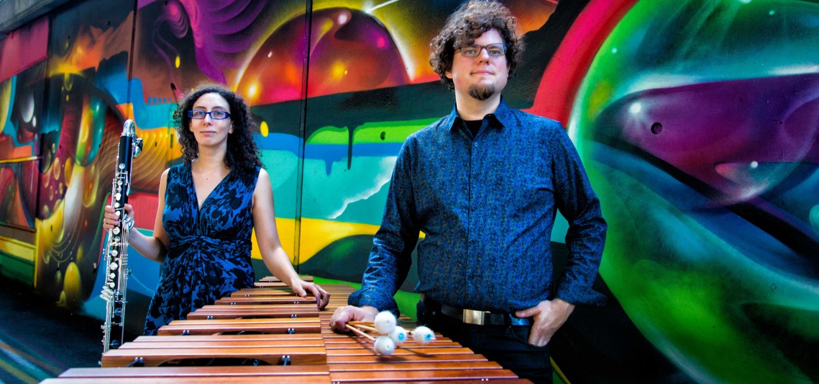 Bass clarinetist Amy Advocat and marimbist Matt Sharrock of Transient Canvas stand with instruments in front of a colorful mural