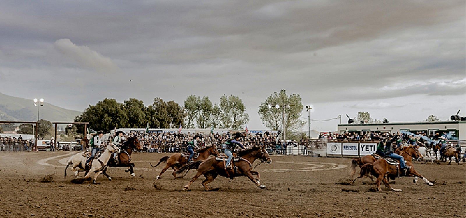 Four pairs of Cal Poly Rodeo women riders circle the area in front of a crowd