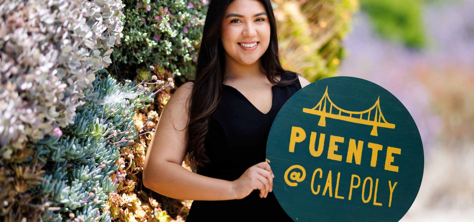 Denis Gonzalez-Reyes holds a sign promoting the Puente @ Cal Poly club, which she founded in 2023