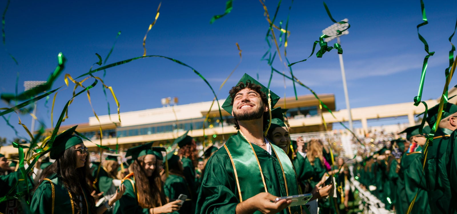 A 2022 Cal Poly graduate smiles as gold and green ribbon floats down