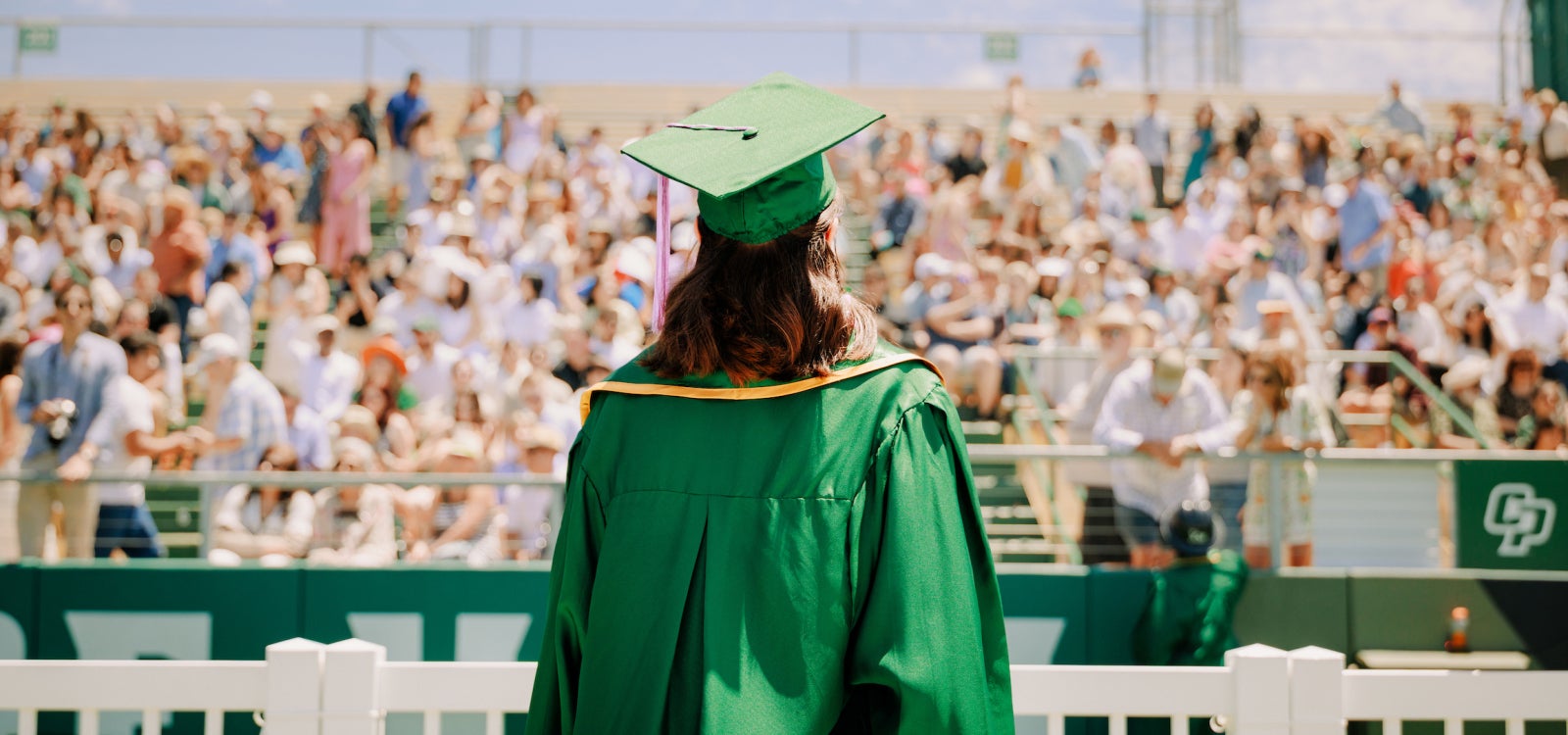 A graduating student from the College of Architecture and Environmental Design faces a stadium crowd gathered for commencement
