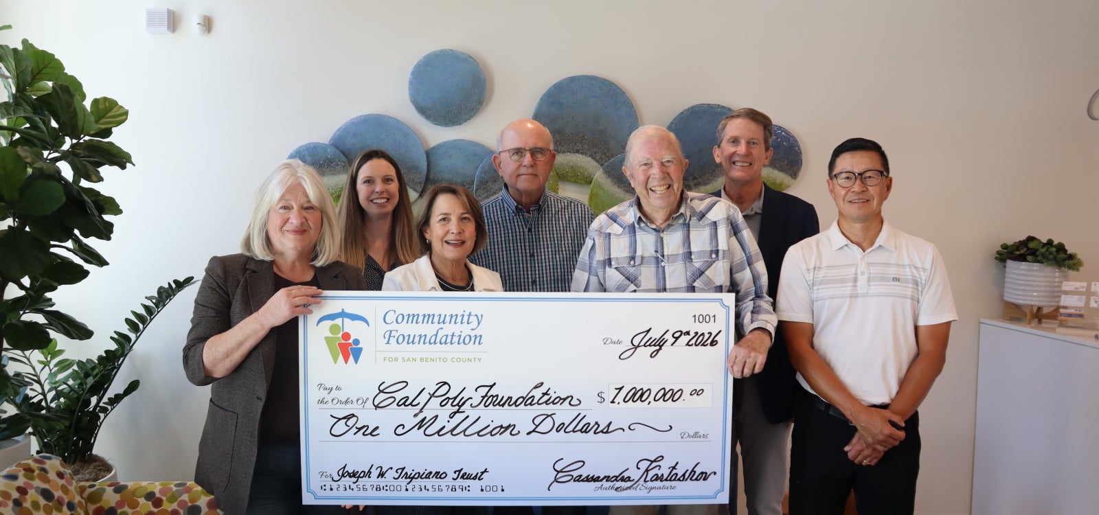 Seven individuals pose with a large check. 