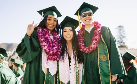 Three student friends smile for the camera after graduating