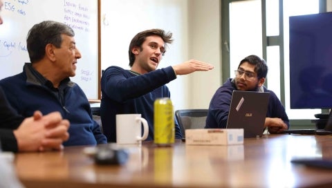 Students gathered around a table discuss their research