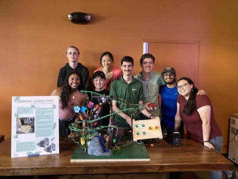 Eight students pose infront of their roller coaster entry and control board