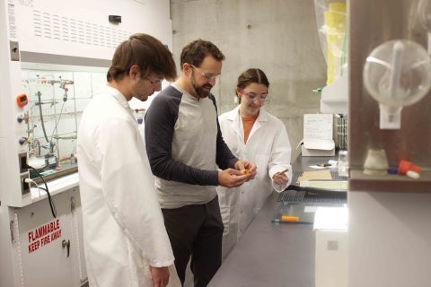 al Poly chemistry Professor Phil Costanzo works in a college lab with two students wearing white lab coats