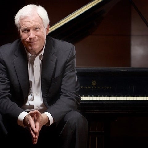 Pianist John Salmon seated on a piano bench with his back to the grand piano