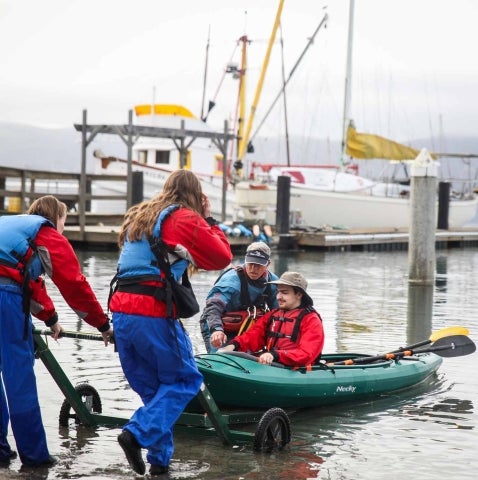 The Adapted Paddling Program support team helps a participant into the water in Morro Bay