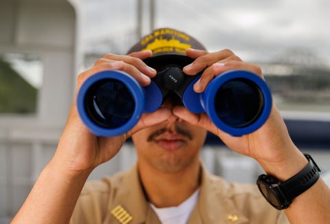 A Cal Poly Maritime Academy cadet uses binoculars aboard the Training Ship Golden Bear