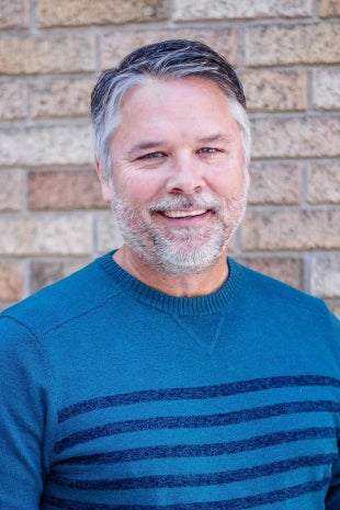 A vertical image of Brian Horga in front of a brick wall