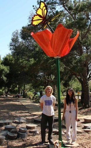 Two students stand with the completed poppy flower and butterfly sculpture