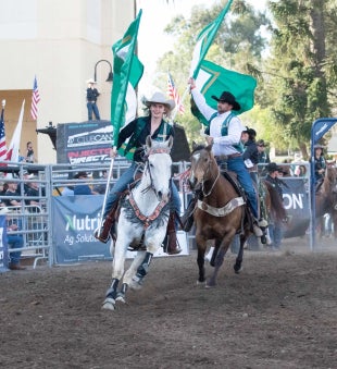 Cal Poly Rodeo team members carry flags spelling Cal Poly as they ride into the rodeo arena