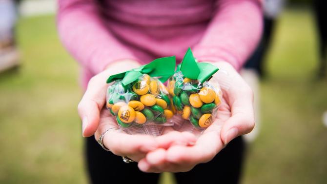 Close-up of small bags of Cal Poly branded green and gold candies in bags being held in a person's hands.