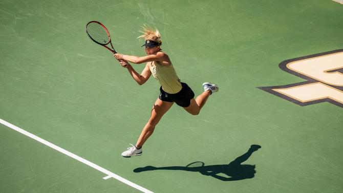 Tennis player runs and reaches with her racket to return a shot.