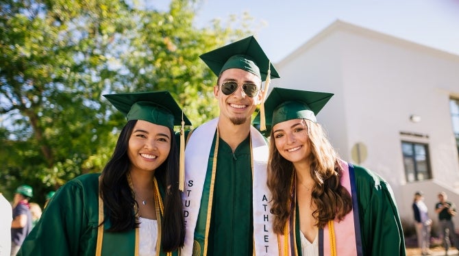 Three students pose after graduation on the Cal Poly campus 