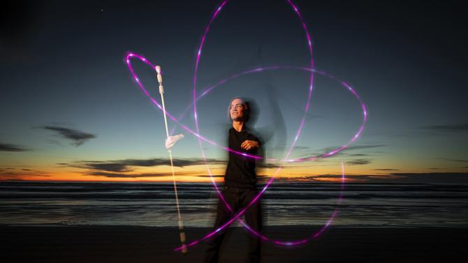 Student spins fire sticks on the beach with the sunset behind them