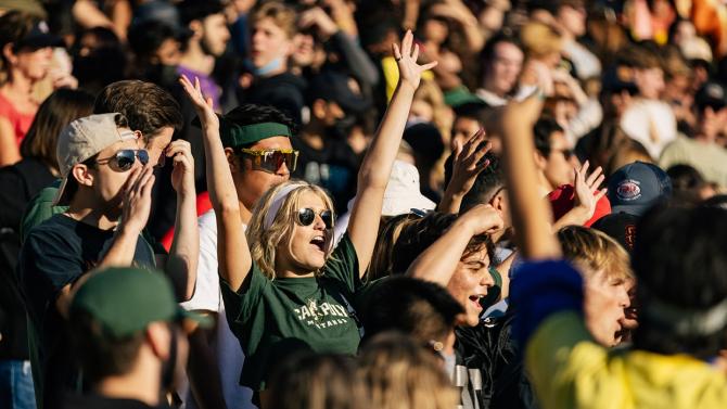 A Cal Poly student in a crowded bleacher cheers for the Mustangs in the outdoor stadium