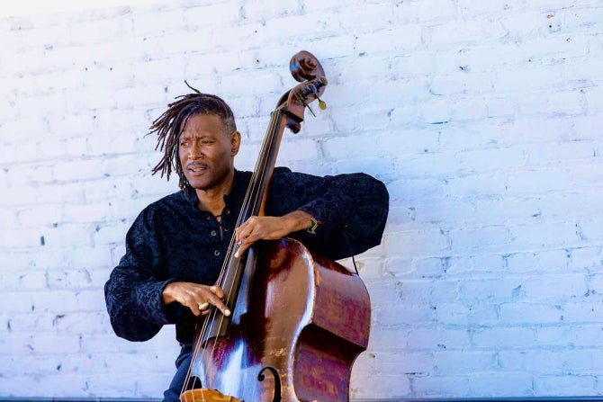 Bay Area bassist, bandleader, composer and educator Marcus Shelby plays bass in front of a white brick wall