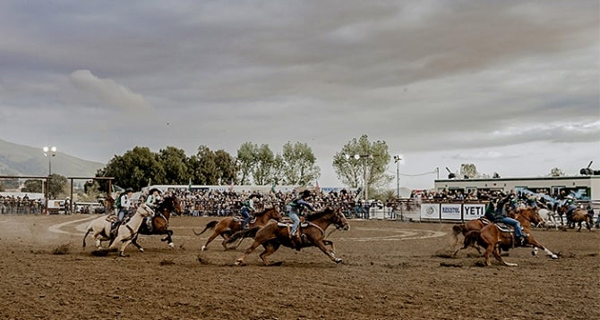 Four pairs of Cal Poly Rodeo women riders circle the area in front of a crowd