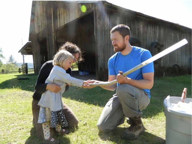A child held by her mother examines the tail of a snake that is in a protective tube held by a man