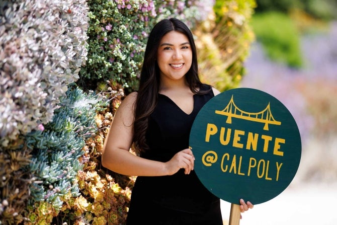 Denis Gonzalez-Reyes holds a sign promoting the Puente @ Cal Poly club, which she founded in 2023