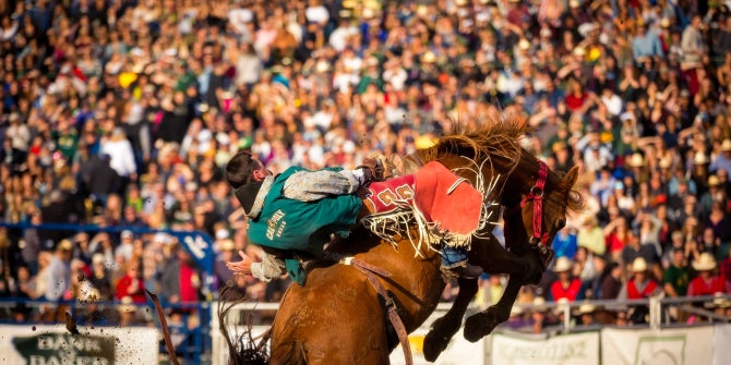 A Cal Poly Rodeo rides a bucking bronc in front of packed grandstands at Spanos Stadium on the Cal Poly campus