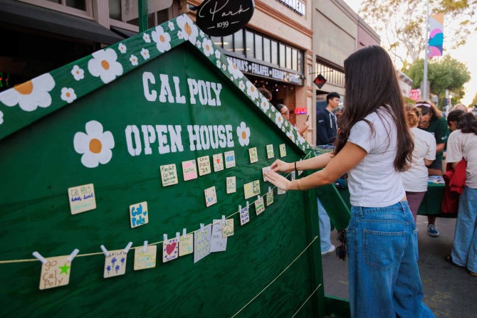 A female students adds to a sign saying Cal Poly Open House