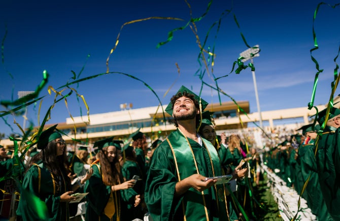 A 2022 Cal Poly graduate smiles as gold and green ribbon floats down