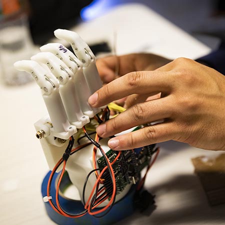 Close-up of a person's hands as they work on a robotic hand model.