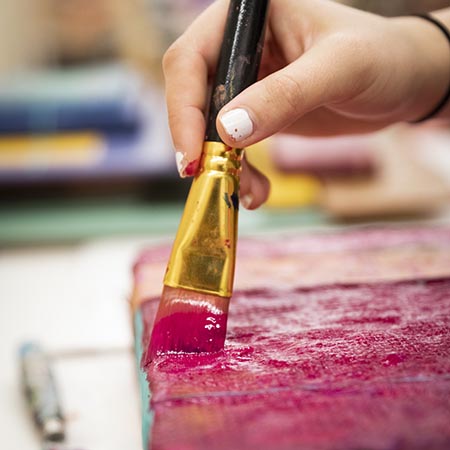Close-up of a person's hand holding a paint brush as they brush paint on a canvas.