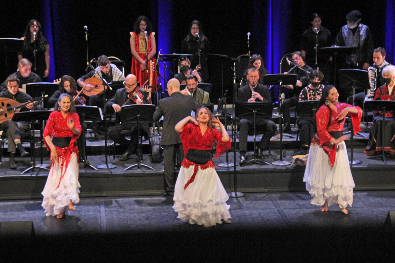 A trio of dancers in colorful costumes dance backed by the Cal Poly Arab Music Ensemble 