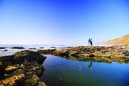 Example of a wide shot with two people standing on rocks at a tide pool, staring out at the ocean. 