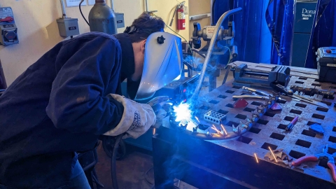 A student welds his CAPED team's roller coaster model