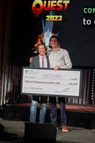 The $15,000 first place winner and a CIE official hold a large 4-foot-long check