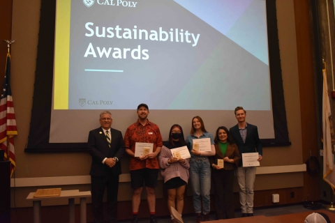 A group displays awards in front of a large screen that says sustainability awards