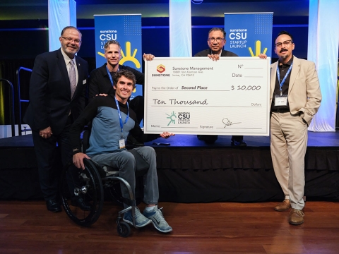 Evan Lalanne, seated in a wheelchair, ggrasps a 5-foot-long replica check for the second-place $10,000 along with representatives of the Sunstone CSU Startup Launch Competition