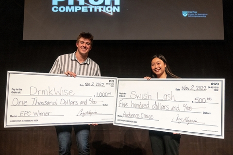 Two students hold large checks won at competition