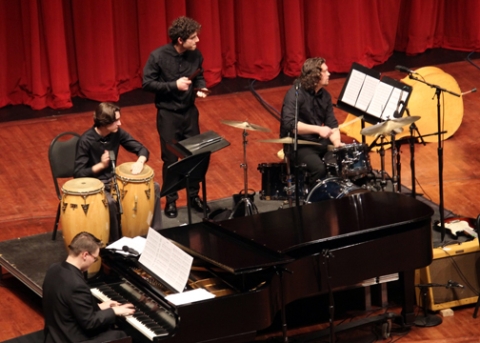 A jazz ensemble features four performers on piano and percussion instruments all looking to their left